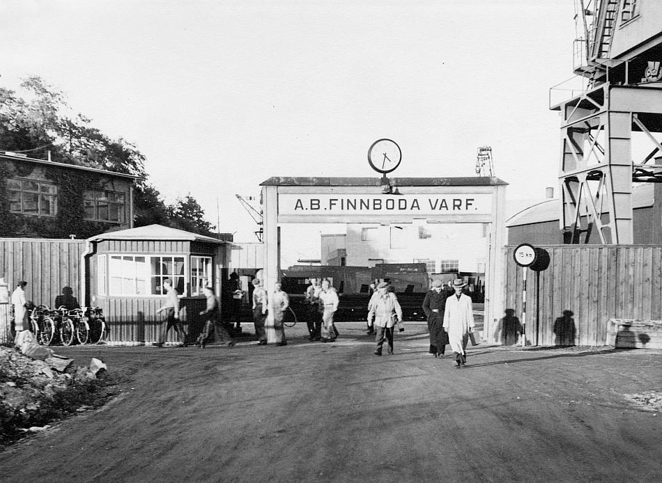 Varvsgrinden vid slutet av en arbetsdag 1948. Till vänster innanför grinden skymtar marketenteriet som idag är kontor och skola. Till höger innanför grinden är platsen för dagens livsmedelsbutik. Foto AFA-Foto. Centrum för näringslivshistoria. NLA