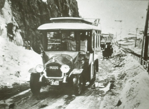 Buss nr 6 är på väg från Södermalm till Björknäs år 1925. Här nedanför Danviksklippan med Saltsjöbanan till höger. Den nybyggda Danviksbron, för både tåg och bilar, skymtar i bakgrunden. Fotograf okänd. Nacka lokalhistoriska arkiv.