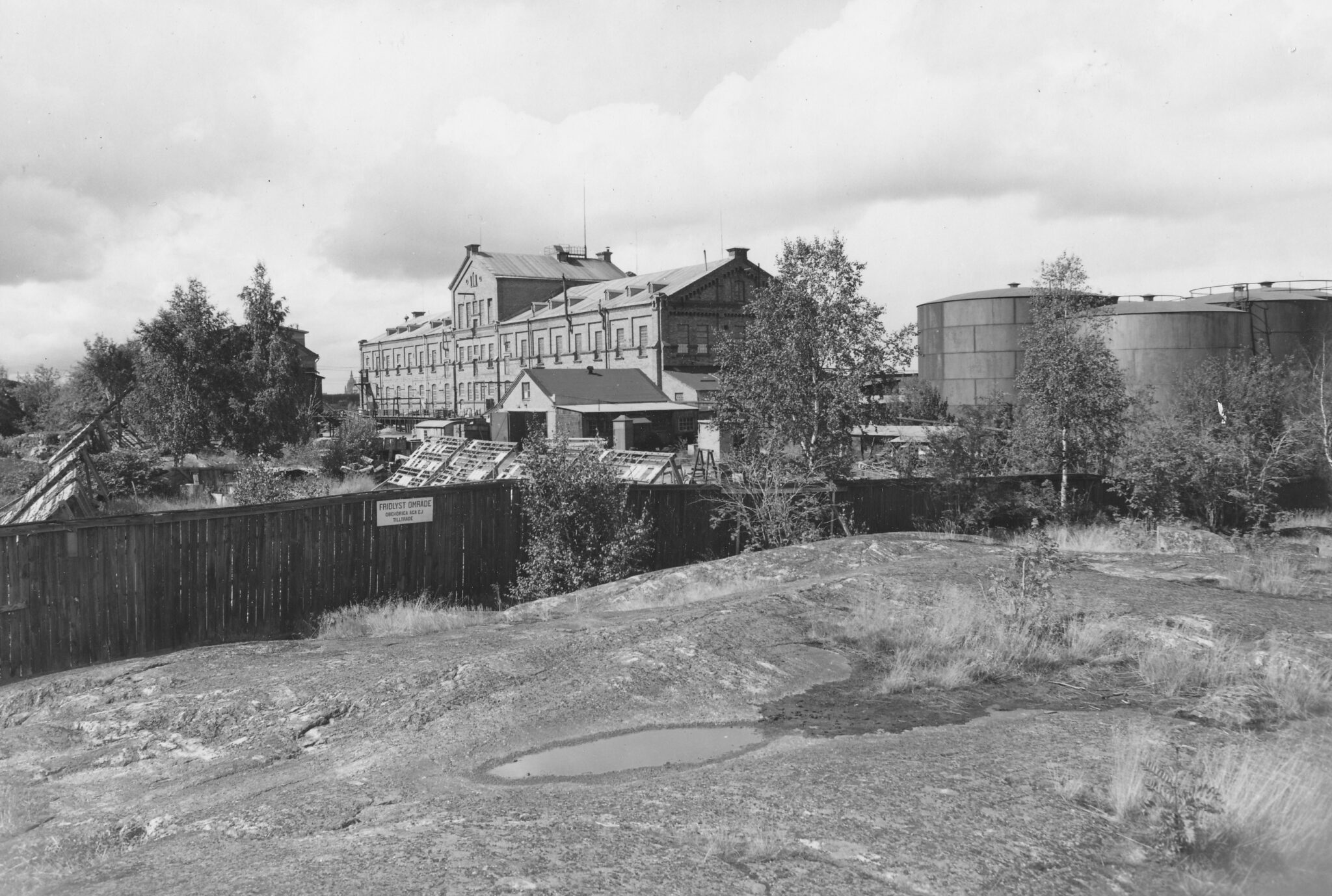 Södersidan av den övre fabriken 1955. Nacka lokalhistoriska arkiv. Fotograf okänd. Bilden är tagen från sydost, bortanför tennisbanan, och fotografen har Kvarnholmsvägen bakom och nedanför sig.
