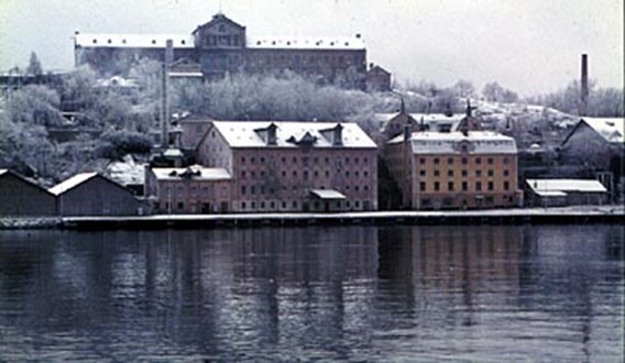 Här syns linoljefabriken på kajen och mattfabriken på klippan. Det gula dårhuset och den låga byggnaden, till höger, som är konstnärsateljé är de enda byggnader som står kvar idag. Foto 1965 av Gunnar Sillén.