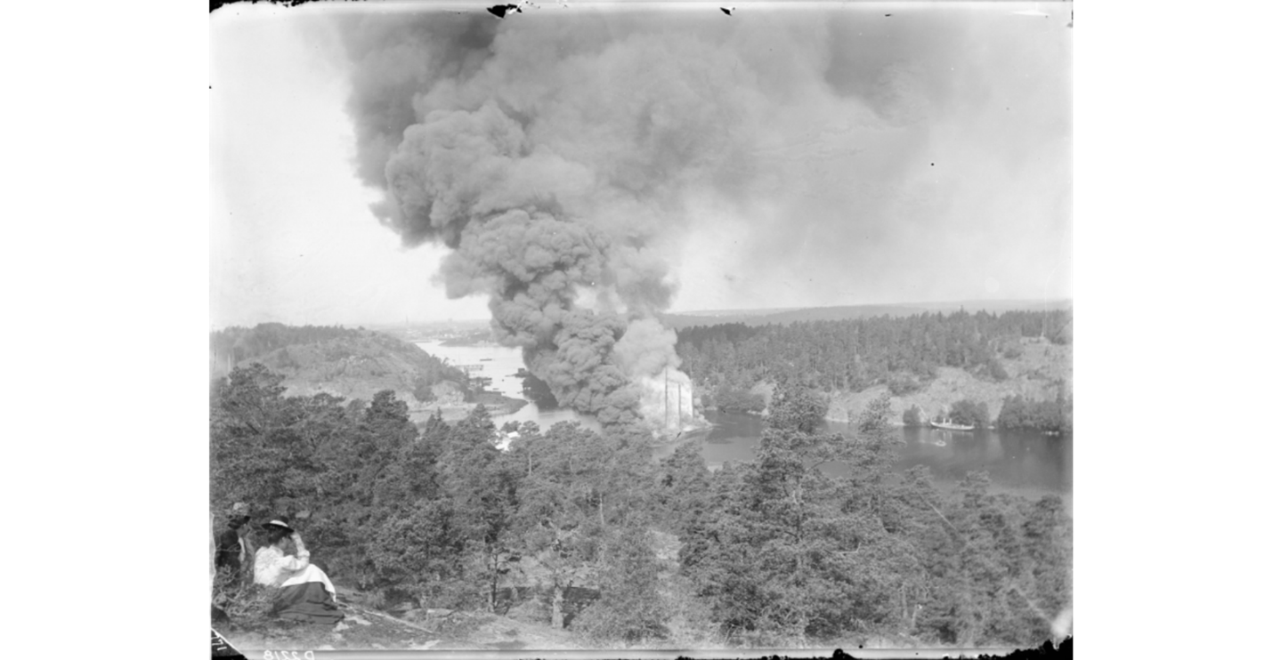 Segelskeppet Louise Adelaide som exploderade sommaren 1901 i Svindersviken med en last av oljeprodukter. På bilden kan man ana masterna i röken. Explosionen inträffade runt 8.30 på morgonen och denna bild togs en timma senare. Olyckan lockade tusentals människor som från bergen runt viken kunde se branden. Det gick till och med extrabåtar från Stockholm med nyfikna. Fotograf M. Befwe. Tekniska muséet.