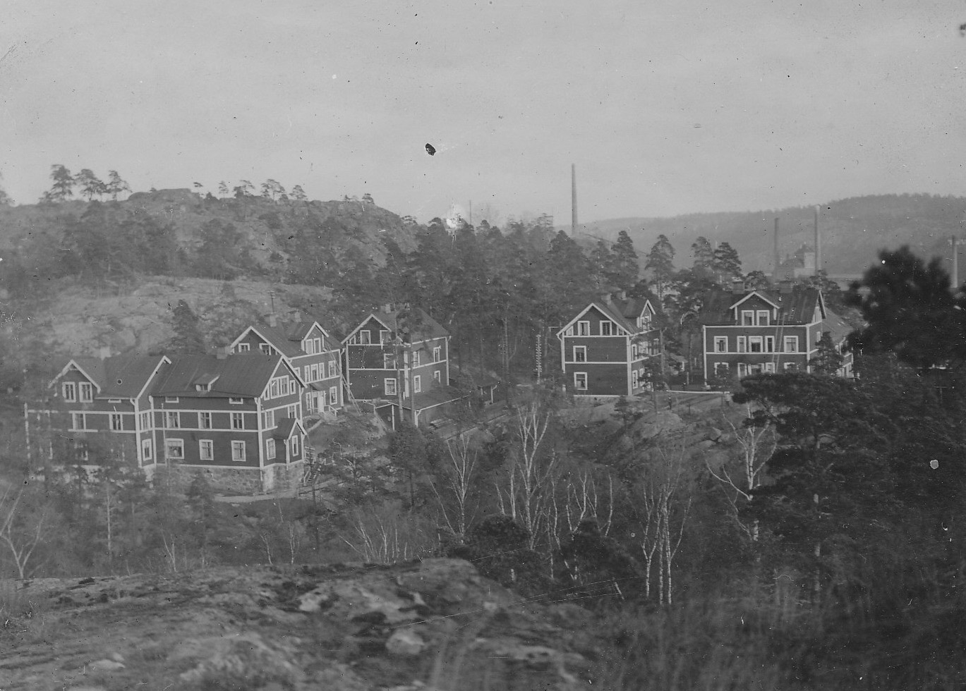 De sex röda husen med arbetarbostäder på Kvarnholmsvägen i början av 1900-talet. Två står kvar idag, mitt emot den gula disponentvillan. Fotograf okänd. Nacka lokalhistoriska arkiv.